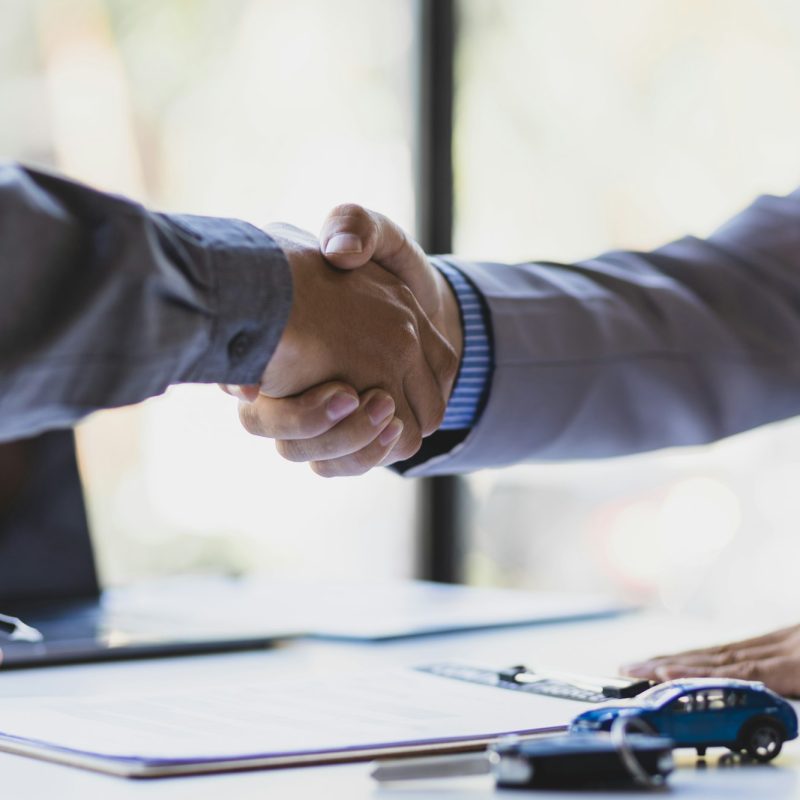 Businessmen shaking hands after signing a car sale with a car salesman.